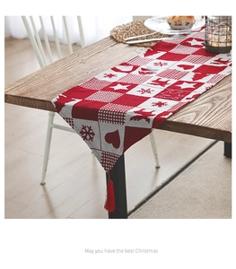 Detail of red and white Christmas table runner with tassels and elk patterns on a wooden table