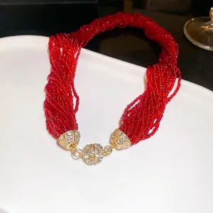 Multilayer red seed bead necklace with gold rhinestone clasp in a white ceramic tray