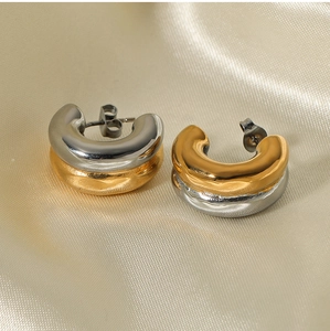 Detail of two-tone C-shape hoop earrings in gold and silver on soft beige silk background