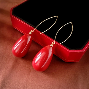 Detail of red teardrop earrings on a velvet jewelry box with elegant gold ear hooks