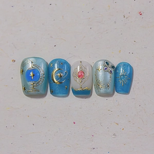 Detail von blauen Cat-Eye-Nägeln mit goldenen Stern-Mond-Mustern und 3D-Anhängern