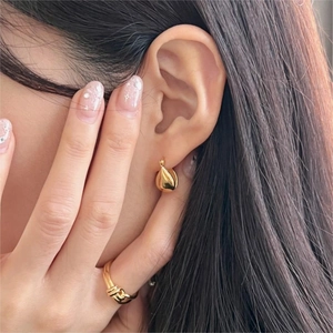 Close-up of elegant gold teardrop earrings and a knotted multi-layer ring on a model