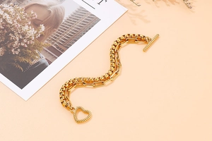 Dettaglio di un bracciale a doppia catena dorata con maglie a scatola e chiusura a cuore OT