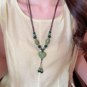 Détail d'un collier pendentif cœur en céramique avec perles vertes et corde tissée