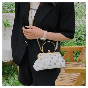 Detail of white embroidered floral shell bag with pearl handle and golden chain