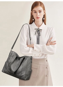 Detail of a large dark grey leather tote bag worn by a model in a professional studio setting