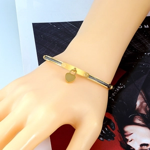 Close-up of gold stainless steel cable bracelet featuring a heart charm on a woman wrist