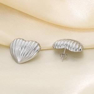 Polished silver heart stud earrings with striped texture on beige silk background