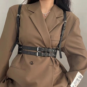 Detail of a black leather harness belt with silver buckles over a brown suit blazer