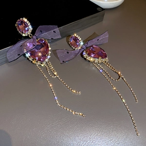Macro detail of purple heart crystal earrings with bow mesh and long gold tassels