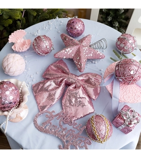 Flat lay of pink Christmas ball ornaments, glitter stars, and bows on a blue cloth background