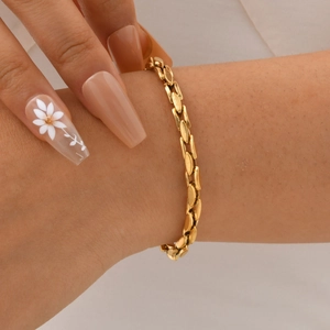 Detail of flat oval gold-tone chain link bracelet on wrist with smooth metallic finish