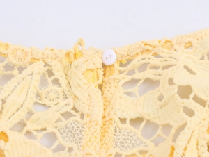 Close-up of elegant yellow lace fabric with intricate hollow patterns and a small white button