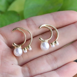 Detail view of gold double crescent moon earrings with white round pearls on hand