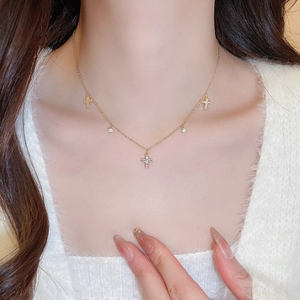 Close-up of a gold necklace with sparkling zircon cross and round charms on a female model