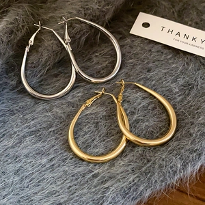 Detailed view of large gold and silver oval drop hoop earrings with polished finish