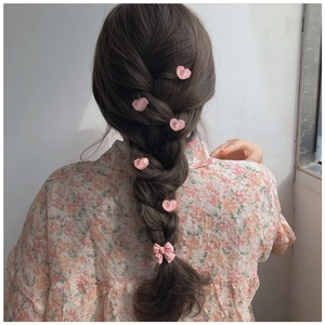 Detail of pink bow and heart hair clips styled in a braided ponytail hairstyle