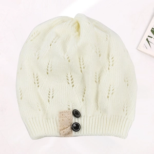Detailed view of the hollow leaf pattern and decorative buttons on white knit beanie