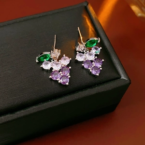 Macro view of purple grape-shaped drop earrings with green leaves on a jewelry box