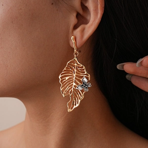 Detail of hollow leaf gold earrings with small silver flower worn by a model
