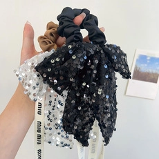 Detailed view of sequin bow scrunchies in black, white, and brown with miumiu branding