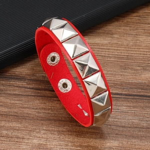 Detail of red leather bracelet with silver pyramid studs on a rustic wooden surface