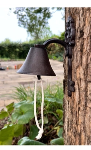 Macro detail of rustic cast iron door bell with woven rope on a textured tree trunk