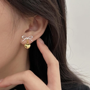 Close-up of model wearing silver bow and gold heart stud earrings in high quality