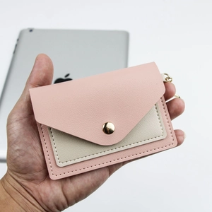 Pink and beige PU leather card holder with snap button closure held by hand