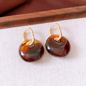 Detail of amber acrylic round pendant earrings with elegant gold square metal clasps