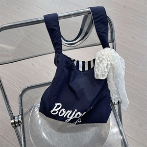 Navy blue canvas tote bag with white Bonjour print and striped strap on a chair