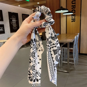 Handheld view of a black and white paisley print silk scrunchie with long ribbons