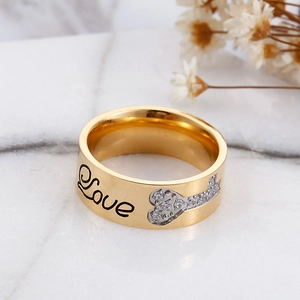 Gold wide band ring with Love engraving and zircon heart key on marble background