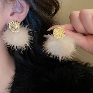 Detail showing golden fan-shaped metal pieces and white plush pom poms on these earrings
