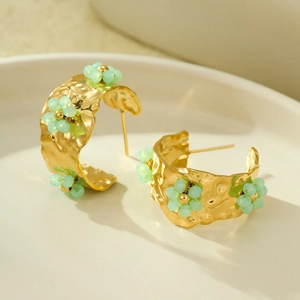 Detail of 18K gold C-shaped earrings with hammered texture and mint green beaded flowers