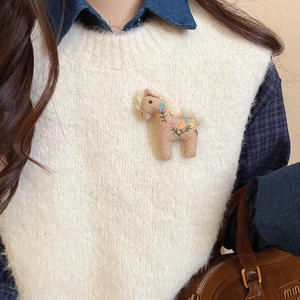 Close-up of beige fabric pony brooch with floral embroidery on white mohair sweater