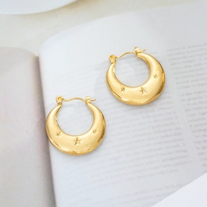Close-up of 18K gold plated crescent earrings with star engraving on white magazine