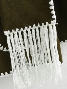 Close-up of olive green fabric with long white tassels and detailed zigzag stitching