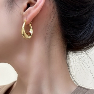 Close-up of elegant gold oval U-shaped drop earrings with a polished mirror finish on model