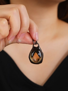 Detail of vintage bronze pendant with translucent brown gemstone held against a dark outfit