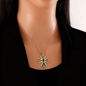 Gros plan d'un collier pendentif croix dorée avec accents bleu foncé porté par un modèle