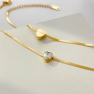 Macro detail of gold snake chain with polished heart and crystal heart charms