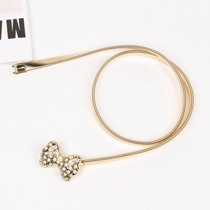 Détail d'une ceinture dorée élastique avec boucle en forme de nœud ornée de strass