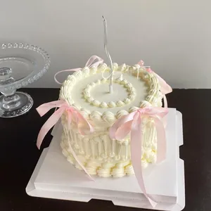 Detailed view of a white cream cake decorated with four elegant pink silk bows and a silver candle
