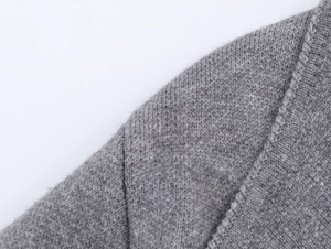 Detail of a grey knitted coat shoulder showing high-quality wool texture and fine stitching