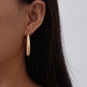 Detail of a smooth golden teardrop earring worn on ear with polished metallic finish