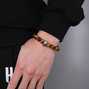 Close-up of tiger eye beaded bracelet with silver skull charm on a male wrist