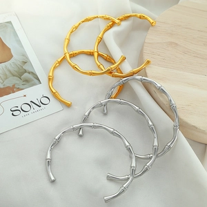 Bamboo style open bangles in gold and silver finish on white fabric setting