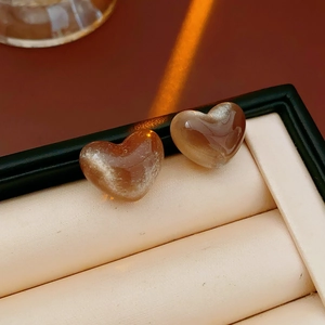 Gros plan de boucles d'oreilles cœur en résine ambrée posées sur un coussin à bijoux