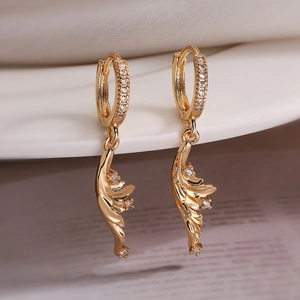 Close-up of golden ginkgo leaf earrings with zircon inlay on white ceramic plate